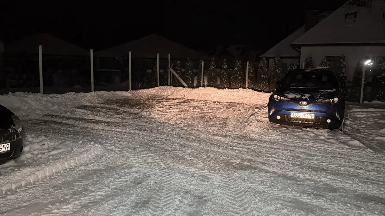 Odśnieżony parking osiedlowy nocą z widocznymi śladami pracy sprzętu zimowego