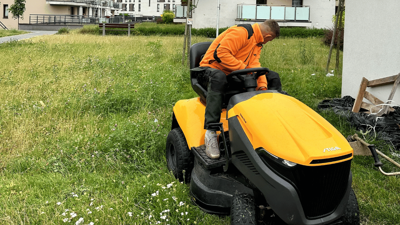 Pracownik koszący wysoką trawę traktorkiem na osiedlu mieszkaniowym