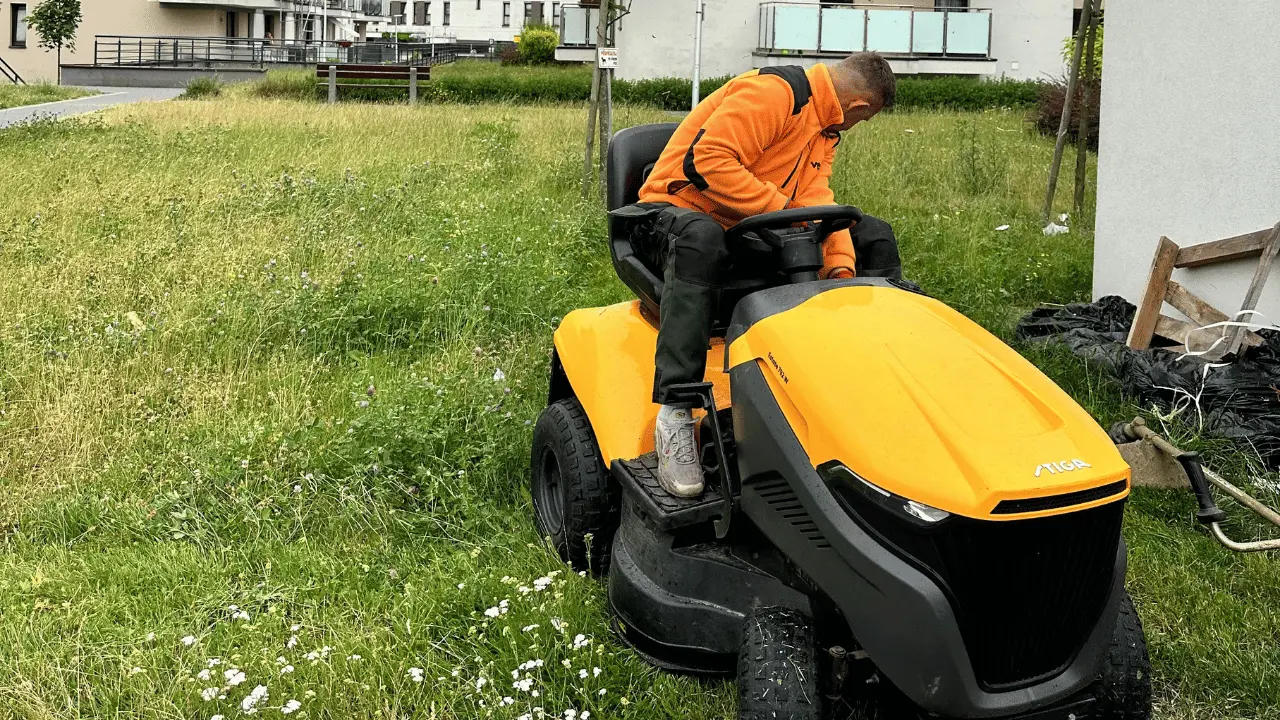 Pracownik koszący wysoką trawę traktorkiem na terenie osiedla mieszkaniowego