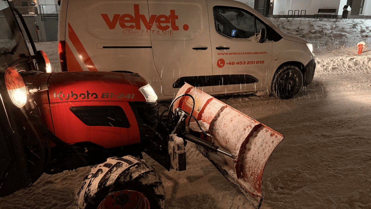 Traktor Kubota z pługiem podczas odśnieżania parkingu obok samochodu Velvet Sprzątanie